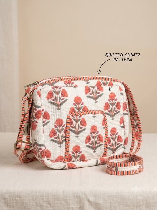 A quilted crossbody bag with a white background and a coral-red and gray floral block print, shown on a neutral beige surface with a text overlay pointing to the quilting pattern.