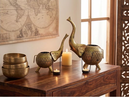 A set of brass decorative elephant figurines and singing bowls arranged on a dark wooden console table in a warmly lit room, with a lit candle and a vintage world map on the wall in the background.