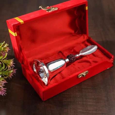 A polished silver-toned metal bell-shaped object with a dark textured neck, presented inside an open red velvet gift box with gold trim, set on a dark wooden surface.