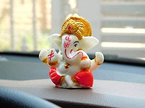 A small idol of Lord Ganesha in white and gold colors, placed on a car dashboard.